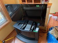 View of RCA 39-inch TV on black Panasonic TV stand with multiple remote controls laying on top