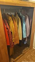 Side view of seven vintage ladies coats on hangers in a wooden closet, showing a range of colors and styles including orange, yellow, brown, and blue.
