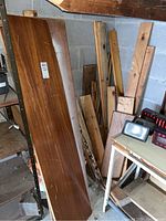 Image showing a large, long finished wooden board along with various smaller wood scraps stacked in corner of garage area.