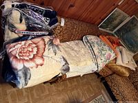 Photo showing the stacked blankets, comforters, and curtains on a couch with wood paneling background.