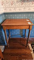Full frontal view of the antique cherry wood writing desk against a floral wallpaper background, showing the rectangular top and spindle legs.