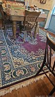 Full view of wool area rug under dining table with floral patterns and fringe.