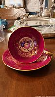 Photo showing front view of the magenta Aynsley teacup with gold designs and fruit motif inside, sitting in matching saucer.