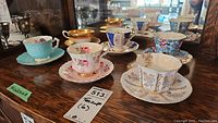 Full set of 6 bone china teacups with matching saucers displayed on wooden surface, showing variety in colors, floral, and gold details.