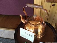 Photo showing full view of copper kettle with wooden handle and lid knob on a small wooden table.