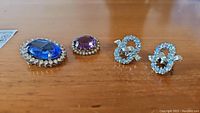 Top view of all five jewelry pieces: two brooches with oval rhinestones and a pair of Coro rhinestone earrings