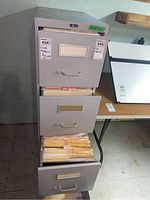 Full view of the gray four-drawer metal filing cabinet with some drawers open to show hanging folders.