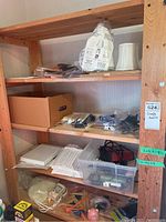 Shelf with assorted craft tools including glue tools, plastic containers with various small items, power cords, and boxed items.
