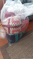 Bag containing multiple crocheted throws including a pink and white crocheted granny square style throw and a blue striped throw.