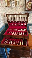 Full view of wood flatware case showing silver flatware organized inside and three mother of pearl handled serving pieces in lower drawer