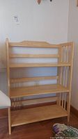 Front view of wooden folding shelf unit showing three shelves and backrest detail, light wood finish.