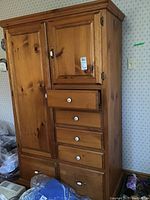 Full frontal photo of pine wood armoire showing entire piece, multiple drawers and one door.