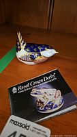 Close-up of the Royal Crown Derby bird paperweight with accompanying certificate/booklet.