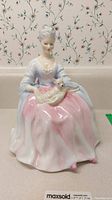 Front view of Royal Doulton Charlotte figurine showing seated woman in pastel 18th-century dress holding a small dog on lap.