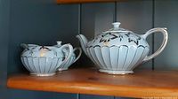 Teapot and sugar bowl side by side on a wooden shelf, showing exterior floral and gold designs.