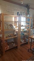 Photo showing two wooden shelving units side by side, each with five shelves, placed in front of curtained window with various small items on shelves.