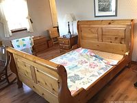 Full view of the pine queen wood bed frame with quilt on it in a bedroom setting showing sleigh style headboard and footboard.