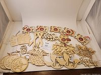 Photo of all 32 wooden Christmas ornaments spread out on flat surface, showing variety of shapes including angels, Joy photo frames, doves, bows, presents, and skis.