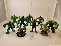 Photo of ten different Hulk figurines with various styles and colors, arranged on white background