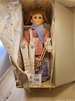Full view of skier doll in original box with skis, poles, ski boot bag, and scarf tucked in.