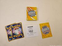 Photo shows the backs of three Pokémon cards and a small stack of cards with the Pokémon World Championships 2009 logo on them. Also shows a MaxSold lot card with lot number 162 and description of 27 Pokémon cards.