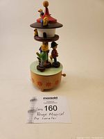 Full side view of the colorful wooden Reuge music box with figurines and winding key visible.