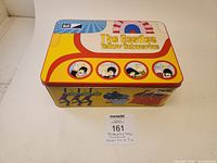 Top and side view of the rectangular tin lunch box featuring The Beatles Yellow Submarine artwork with band member portraits and colorful psychedelic design.