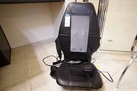 Full view of Homedics massage chair pad in black leather-like material on floor, with attached wired handheld controller and power cord visible.