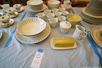 Overview of the china set including plates, bowls, cups, butter dish, sugar bowl, and creamer, arranged on light blue cloth.