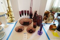 Assortment of purple glassware including decanters, vases, glasses, and plates displayed on a table.