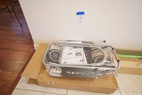 Full view of unopened Trolley Dolly in packaging on top of a cardboard box with some parts, frame and wheels visible.