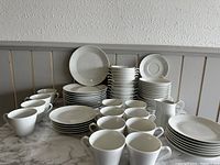 Overview of all dishes showing stacks of plates, cups, saucers, and creamer jug, arranged on marble surface against paneled wall.