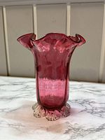 Front angled view of cranberry glass vase with applied crimped feet and ruffled opening
