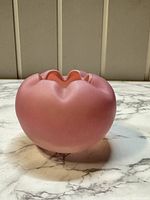 Side view of matte pink rosebud vase with cinched opening showing smooth rounded body on marble surface.