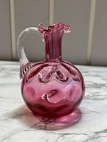 Front side of the Fenton ruby cranberry overlay glass decanter showing polka dot textured round body, ruffled top, and clear handle.