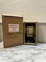 Photo of the light up hanging picture frame next to the original box labeled Framagic breakable glass.