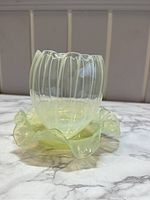 Side view showing the ribbed glass bowl with ruffled flared base and opalescent translucency, placed on a marble surface.