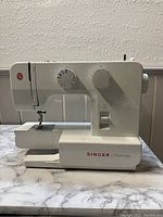 Front and side/front view showing Singer Promise sewing machine with two adjustment dials, needle area and markings on the base.