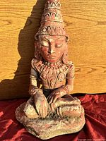 Front view of the sitting Buddha statue showing detailed facial features, crown, and ornamental jewelry with reddish worn paint.