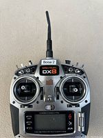 Front view of Spektrum DX8 remote controller transmitter showing joysticks, control switches, digital display, and antenna.