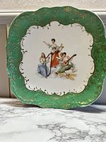 Front view of the Victoria Carlsbad Austria decorative plate showing three women playing musical instruments with green, gold embellished border.