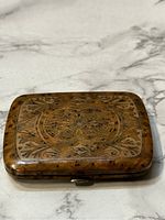 Photo showing front of vintage Bakelite cigarette case with carved intricate floral and geometric designs.