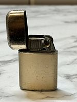 Side view of the vintage Ronson Typhoon lighter with lid open showing metal body, striker wheel, and ignition mechanism.