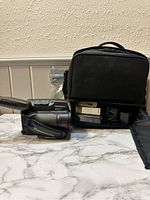 Panasonic video camera positioned next to a black carrying case with accessories visible inside.