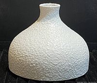 Side view showing textured bulbous white ceramic vase with narrow neck and small opening.