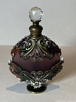 Front view of frosted glass perfume bottle with ornate enamel and crystal decoration, topped with faceted crystal stopper.