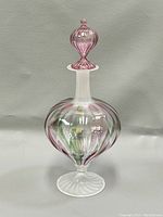 Front view of blown glass perfume bottle with pink and green swirled pattern, frosted white neck and foot, and matching stopper on top.