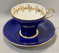 Front view of Aynsley teacup and saucer, showing cobalt blue color with gold filigree detail inside the cup and gold trim on edges.
