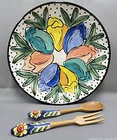 Front view of the serving bowl with floral tulip design and the wooden serving spoon and fork with hand-painted ceramic handles laying in front.