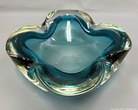 Top view of a blue-tinted thick glass ashtray with clear glass edges showing organically curved and petal-shaped rim.